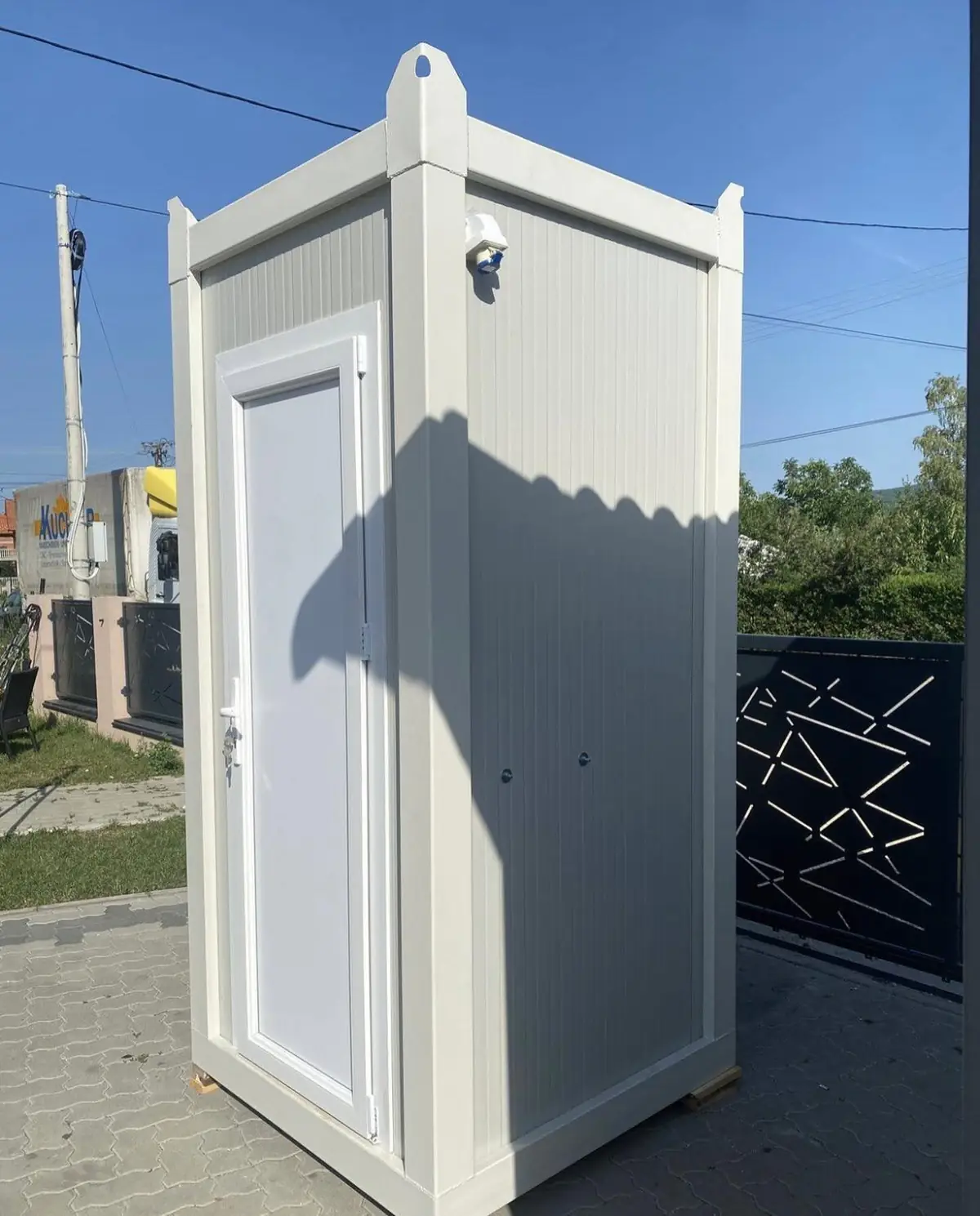 White flushing restroom cabin beside a home driveway gate