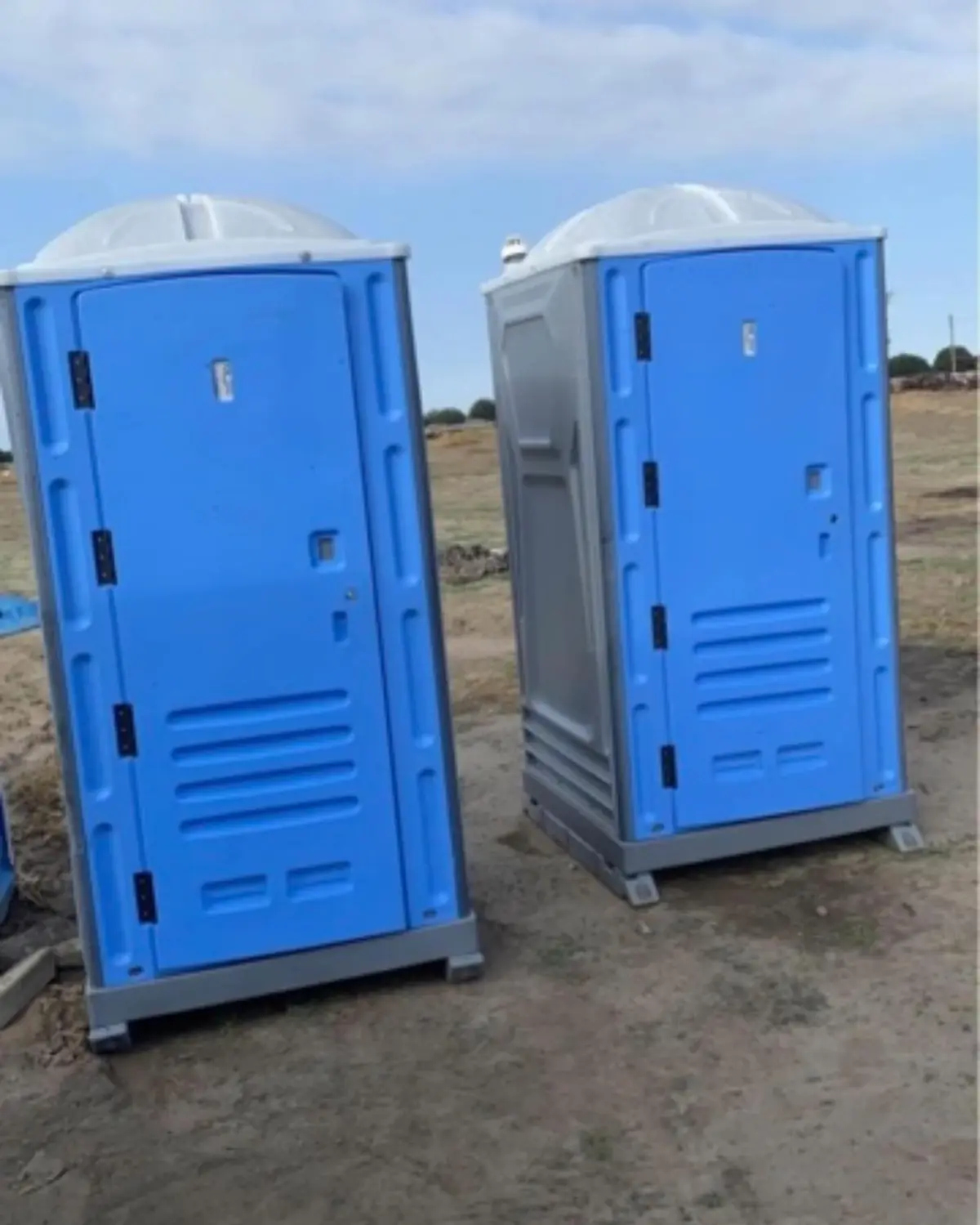 Two blue standard porta potties delivered to an open dirt job site